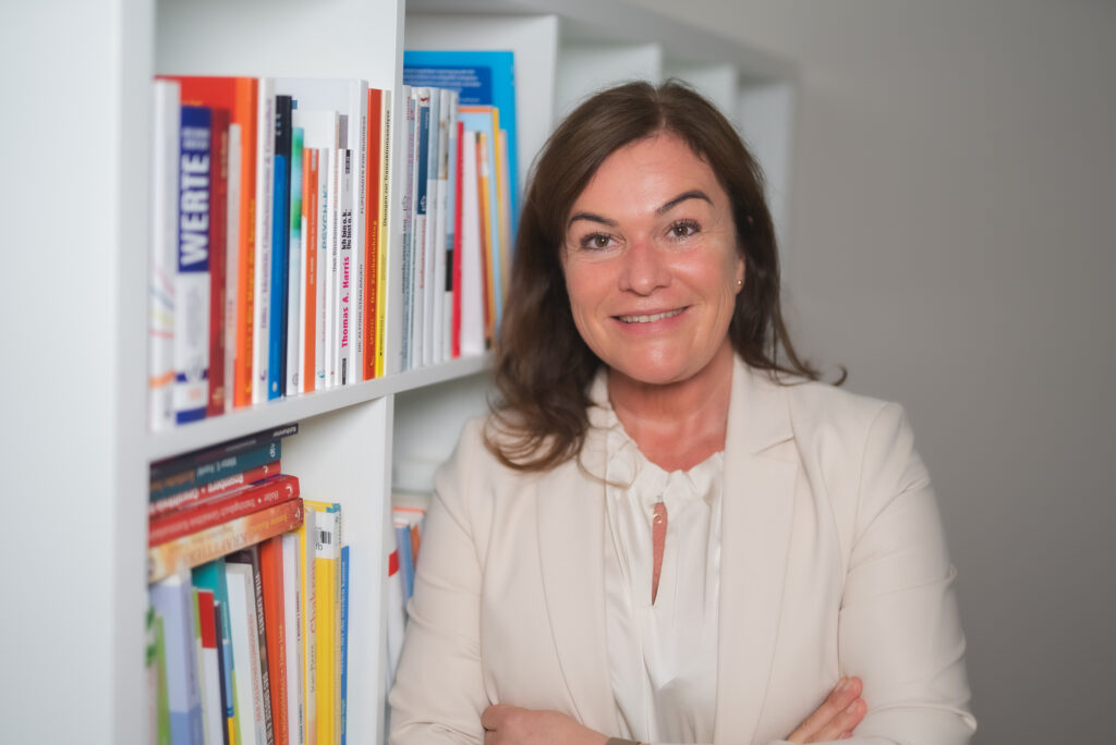 Frau steht lächelnd vor Bücherregal im Büro