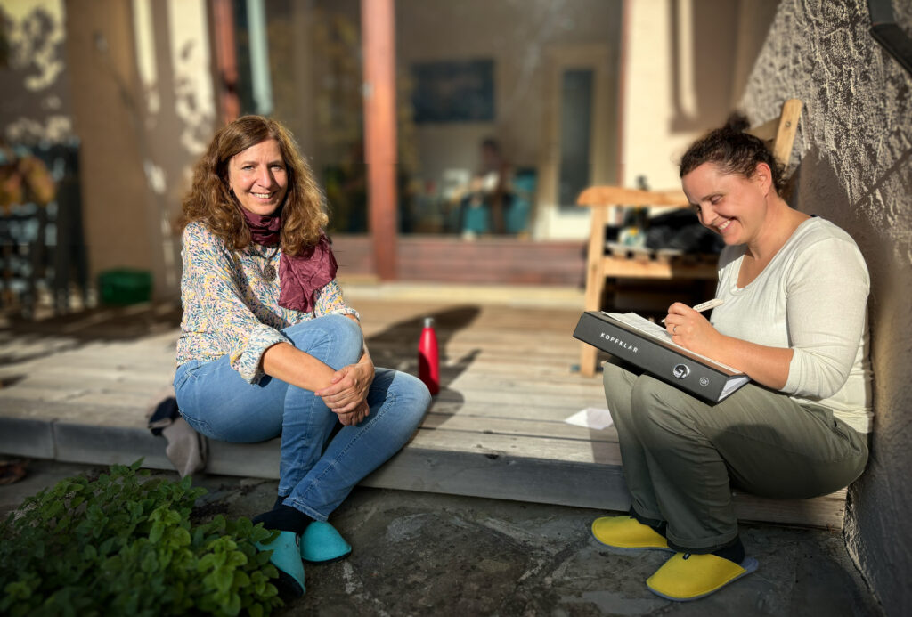 Zwei Frauen sitzen auf einer Terrasse im Sonnenlicht.